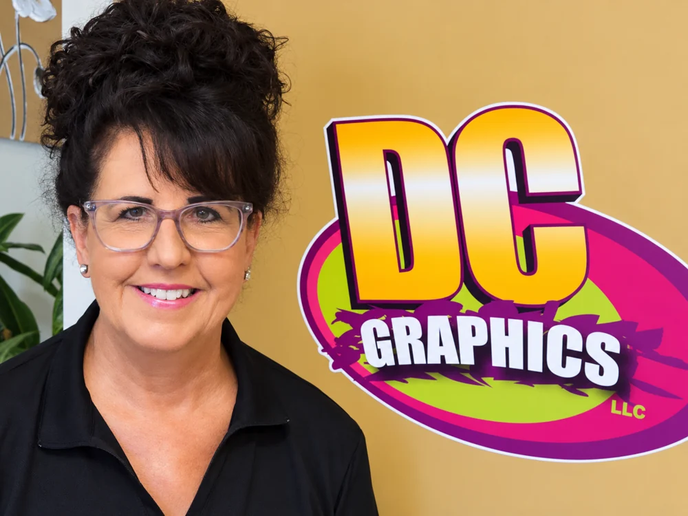 Denise Christenson, founder of DC Graphics, beside the DC Graphics logo