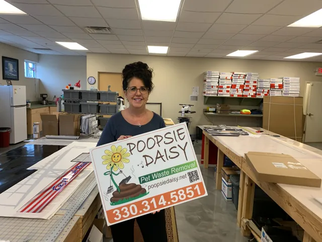 Custom yard sign held by Denise in the shop